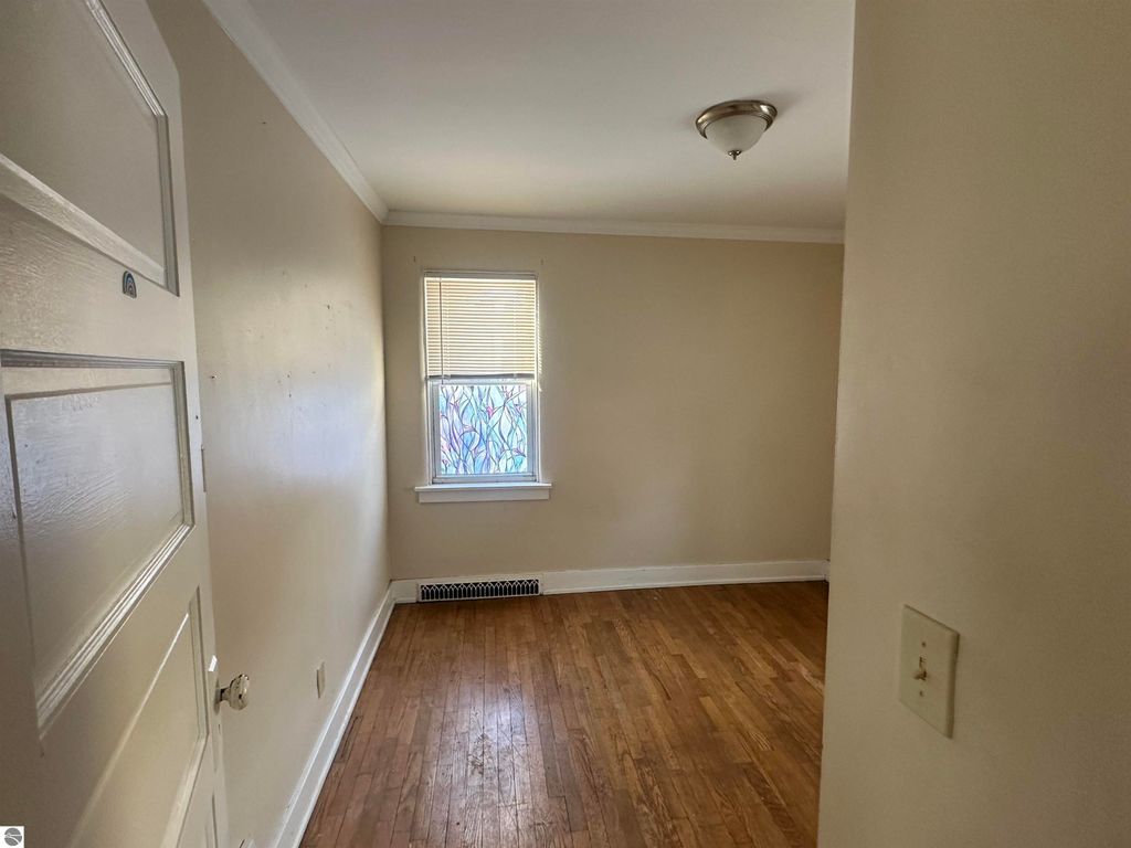 Cozy interior view of 110 W State Street, Clare, MI, featuring hardwood flooring, a window with blinds, and light-colored walls, highlighting the charm of this 2-bedroom, 1-bath home for sale.