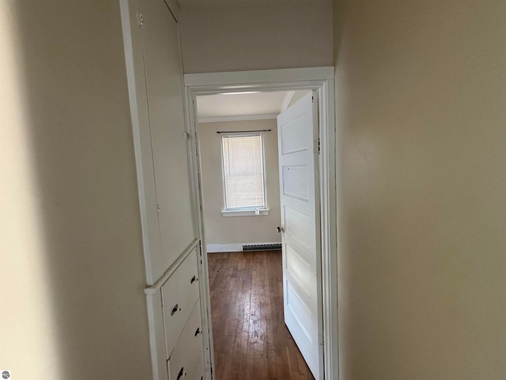 Hallway view of a cozy 2-bedroom home in Clare, MI, featuring hardwood floors, built-in storage, and natural light from a window.