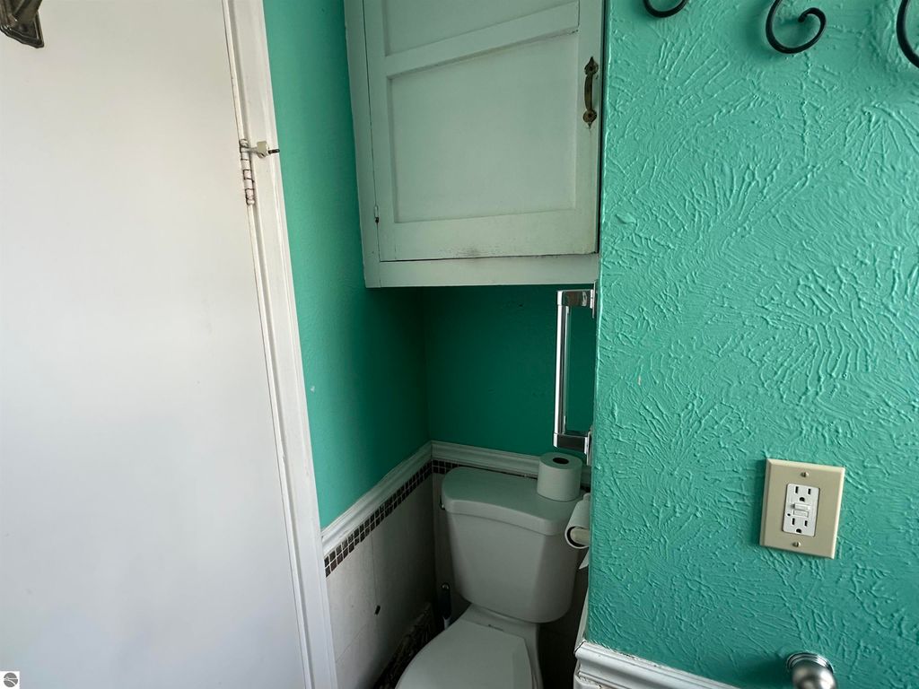 Bathroom corner featuring a turquoise wall, toilet, and a white cabinet above, showcasing a cozy and colorful interior design.