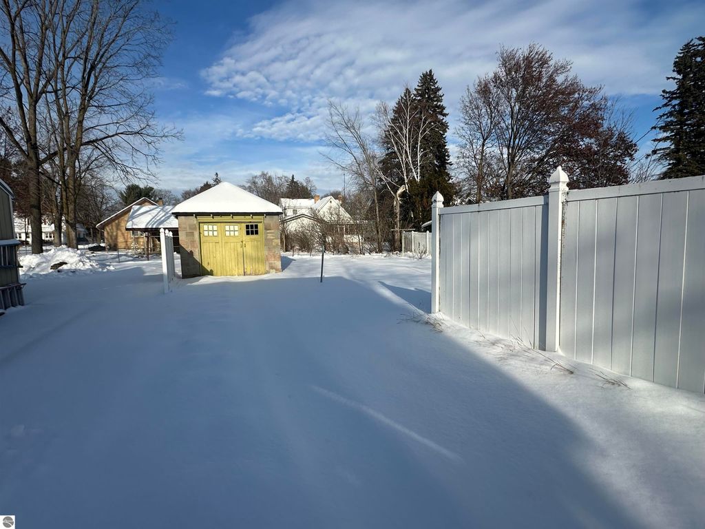 Snow-covered backyard with a small yellow shed, white fence, and trees in Clare, MI, showcasing the outdoor space of the 2-bedroom home for sale at 110 W State Street.