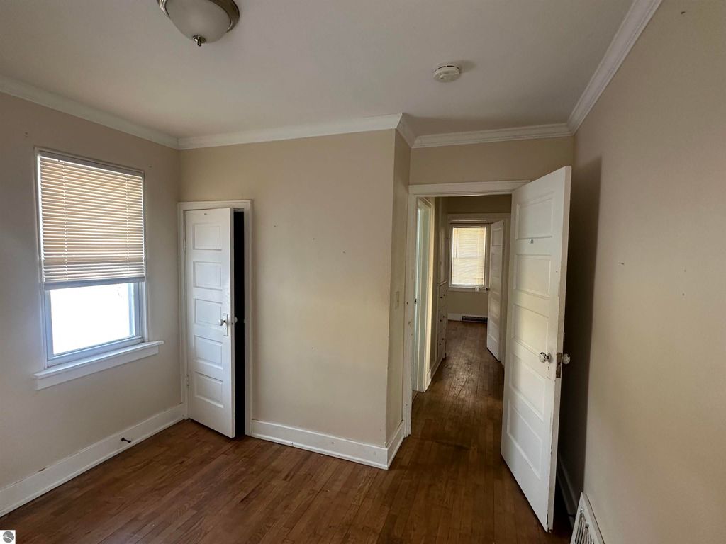 Interior view of cozy 2-bedroom home at 110 W State Street, Clare, MI, featuring hardwood flooring, multiple doors leading to adjacent rooms, and natural light from window.