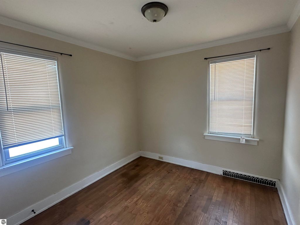 Cozy interior of a 2-bedroom home featuring hardwood flooring, two windows with blinds, and neutral wall colors, showcasing the inviting atmosphere near downtown Clare, MI.