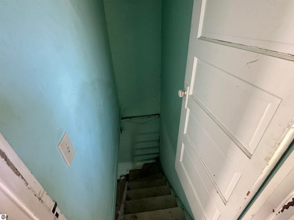 Staircase leading to a basement with mint green walls and a white door, part of the 2-bedroom home at 110 W State Street, Clare, MI.