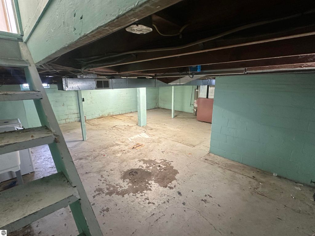 Basement interior of a 2-bedroom home at 110 W State Street, Clare, MI, featuring exposed beams, concrete flooring, and green painted walls.