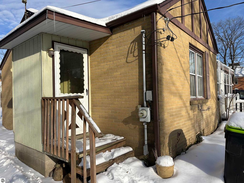 Charming exterior view of a 2-bedroom home at 110 W State Street, Clare, MI, featuring a wooden porch, brick facade, and snow-covered yard.