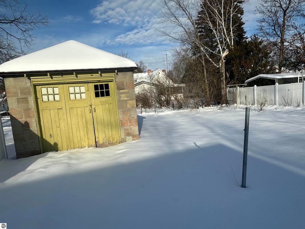 Small green detached garage surrounded by snow in Clare, MI, with a clear sky and trees in the background, highlighting the property's outdoor space.
