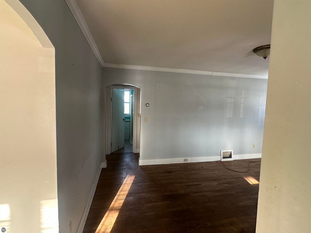 Interior view of a 2-bedroom home at 110 W State Street, Clare, MI, featuring hardwood flooring, gray walls, and an entryway leading to a bathroom, showcasing the property's cozy and classic character.