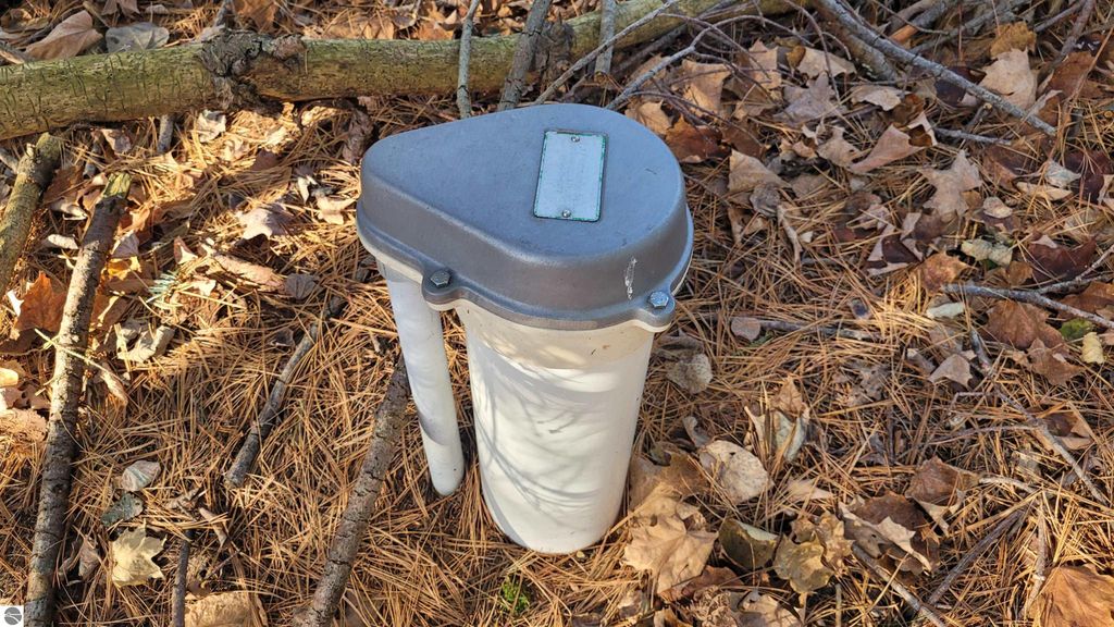 Well and septic system cover in wooded area with fallen leaves, indicating outdoor recreational potential of 40-acre property near Alden, MI.