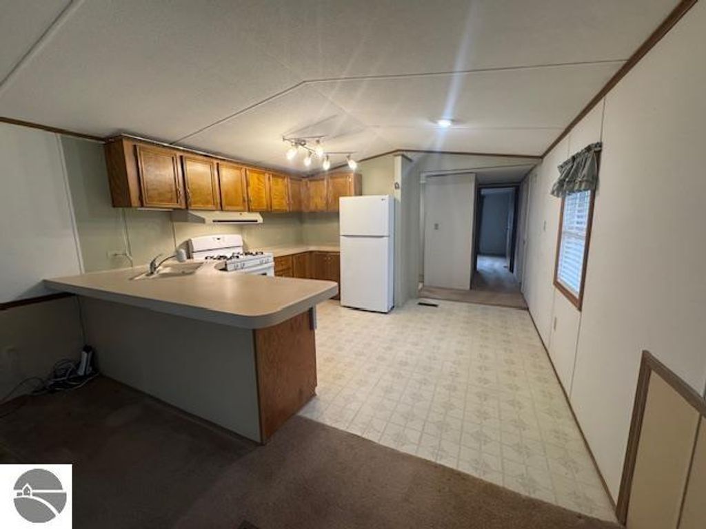 Interior view of a well-maintained kitchen in a 3-bedroom home for sale at 2520 S Blodgett, Lake City, MI, featuring wooden cabinets, a gas stove, and a white refrigerator, with a carpeted living area visible in the background.