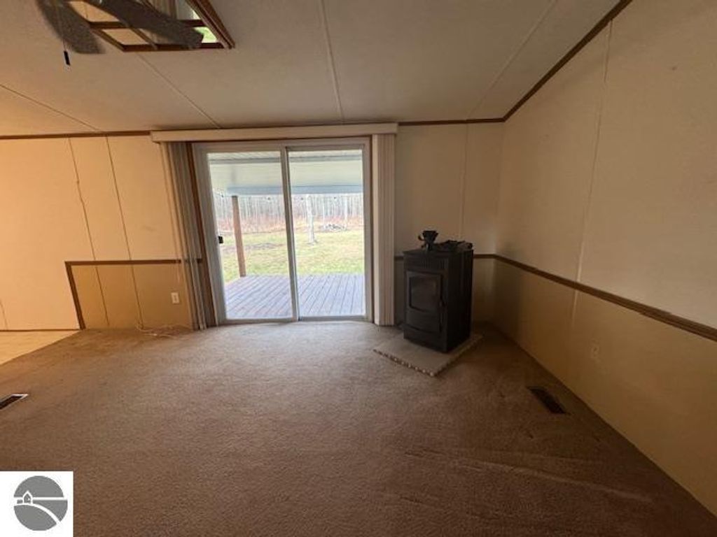 Interior view of a well-maintained living room featuring a pellet stove, sliding glass door leading to the outdoor area, and carpeted flooring, showcasing the cozy atmosphere of the 3-bedroom home for sale at 2520 S Blodgett, Lake City, MI.