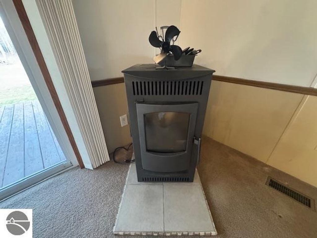 Pellet stove in living area of well-maintained 3-bedroom home at 2520 S Blodgett, Lake City, MI, featuring carpeted flooring and natural light from adjacent sliding door.