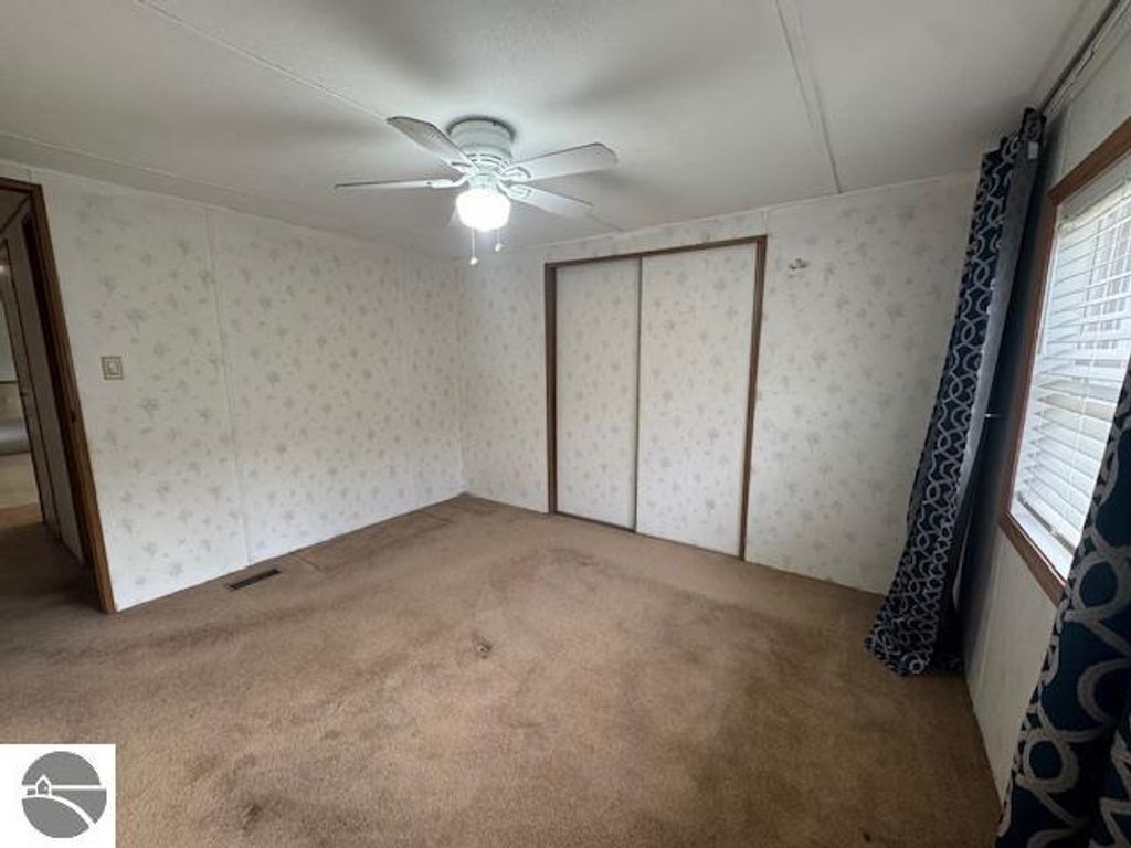 Interior view of a well-maintained room in a 3-bedroom home with carpeted flooring, ceiling fan, and floral wallpaper, showcasing the spacious layout and natural light from the window, relevant to the Lake City, MI real estate listing.