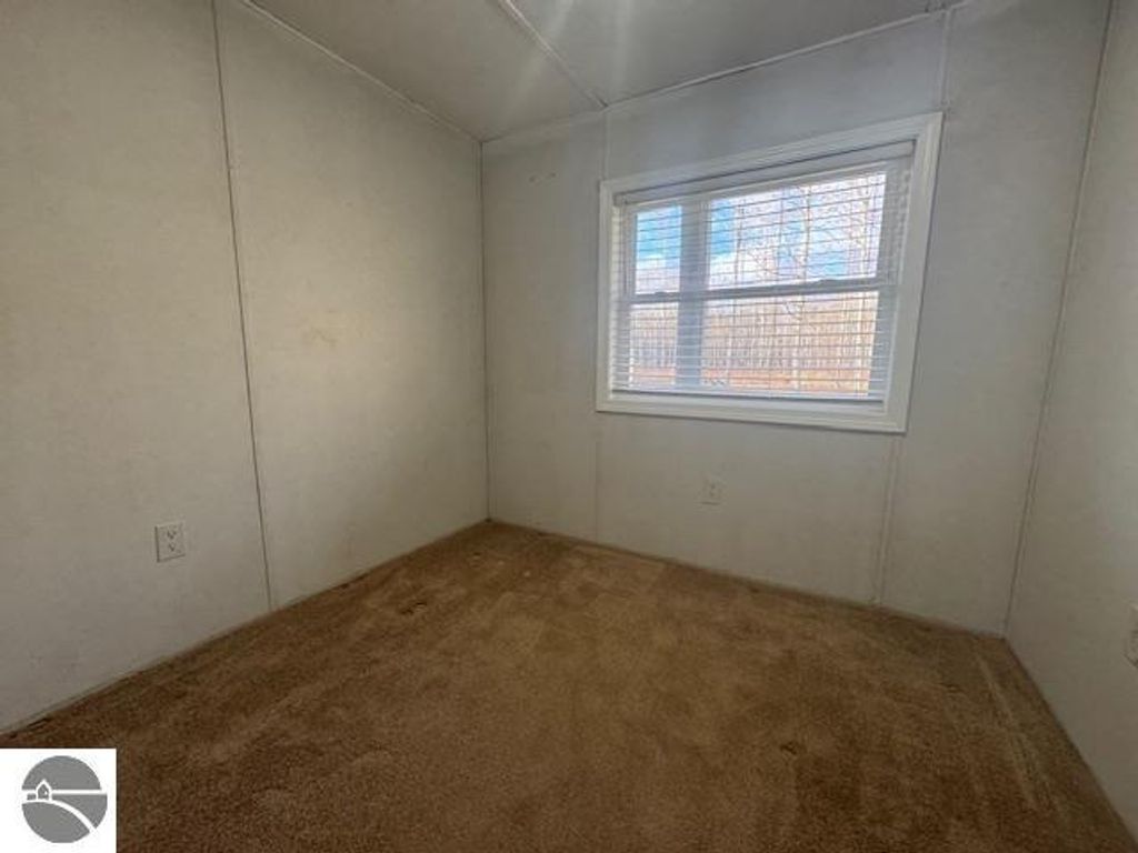 Interior view of a vacant bedroom with beige carpet, white walls, and a window allowing natural light, part of a 3-bedroom home for sale in Lake City, MI.