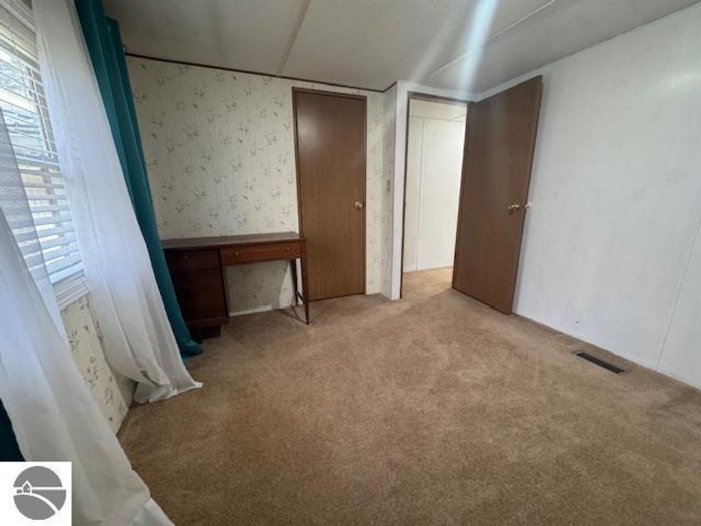 Interior view of a well-maintained room in a 3-bedroom, 1-bath home for sale at 2520 S Blodgett, Lake City, MI, featuring beige carpet, floral wallpaper, a wooden desk, and two closed doors.