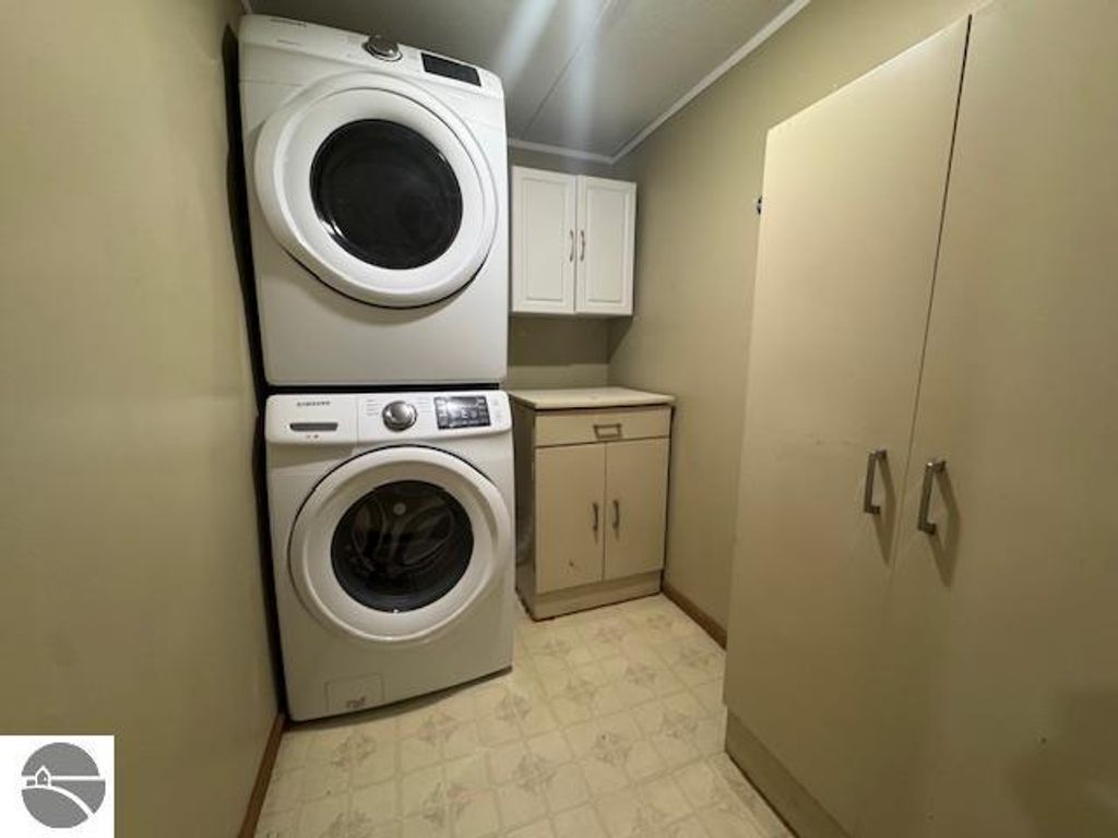 Washer and dryer stacked in a laundry room with beige walls, storage cabinets, and a countertop, highlighting home maintenance features relevant to the listing at 2520 S Blodgett, Lake City, MI.