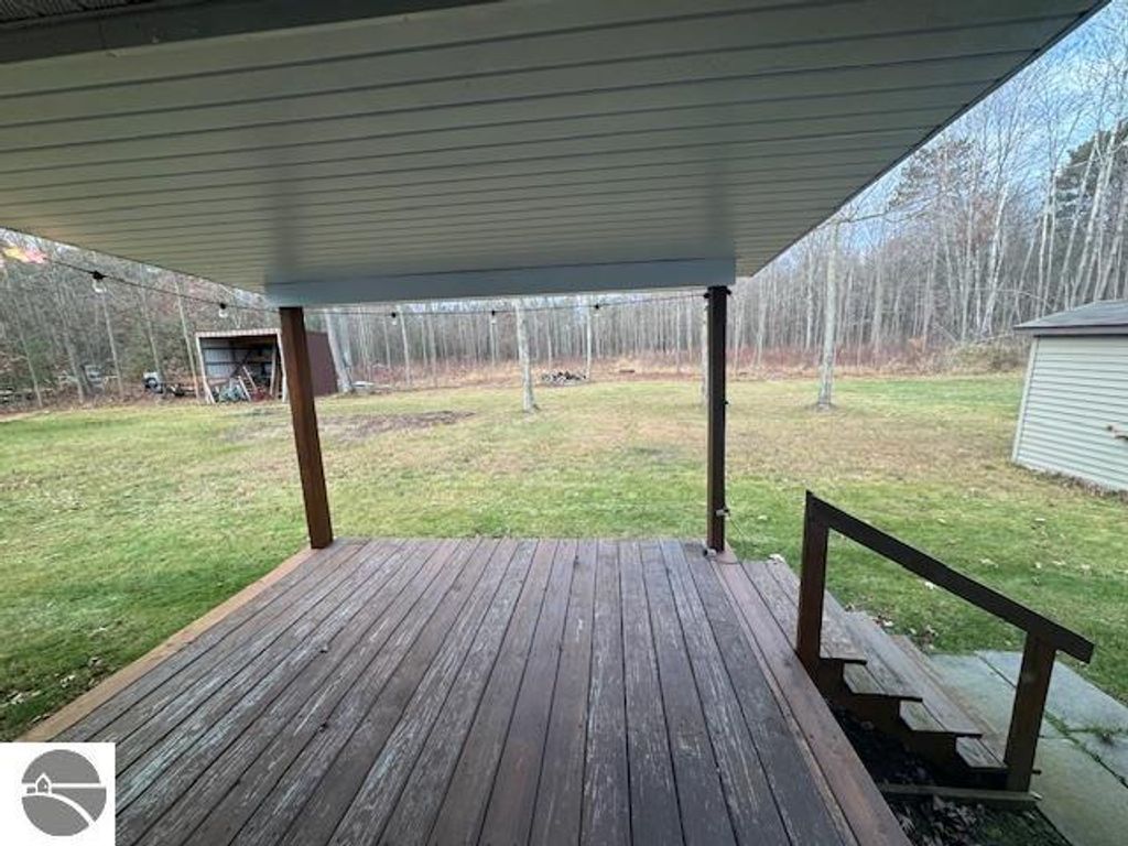 Wooden deck view with steps leading to a spacious backyard, featuring a large grassy area and trees, showcasing the outdoor space of a 3-bedroom home in Lake City, MI.