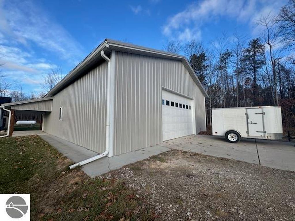 Pole barn with garage door, concrete driveway, and trailer, set on 2.5 acres near Lake City, MI.