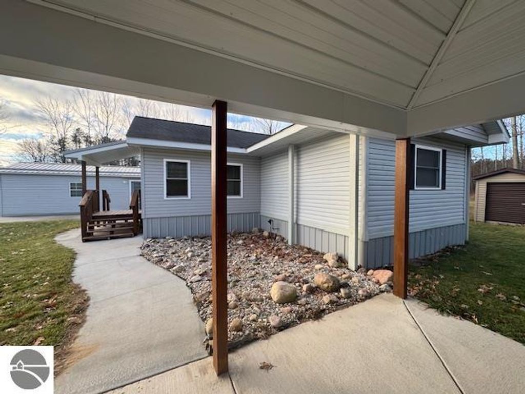 Well-maintained home exterior at 2520 S Blodgett, Lake City, MI, featuring a concrete walkway, landscaped stones, and a wooden porch leading to the entrance.