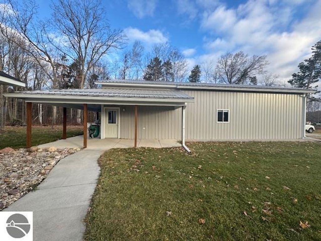 Well-maintained pole barn with a metal exterior, concrete walkway, and surrounding trees, located on 2.5 acres in Lake City, MI, as part of a real estate listing for a 3-bedroom home.