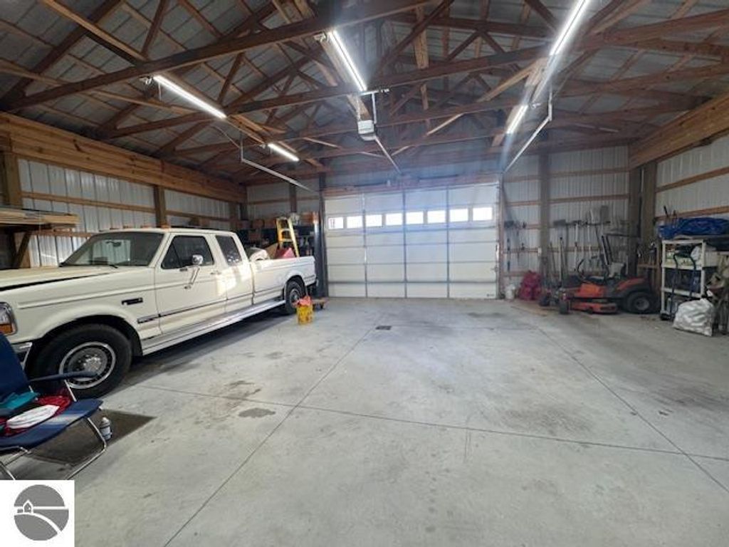 Interior of a spacious pole barn featuring a white pickup truck, concrete flooring, and various tools stored along the walls, highlighting the property's ample storage options at 2520 S Blodgett, Lake City, MI.