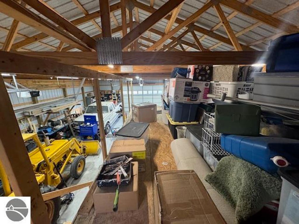 Interior view of a spacious pole barn filled with storage boxes, tools, and equipment, showcasing the organized space for vehicles and a loft area, relevant to the Lake City, MI property listing at 2520 S Blodgett.