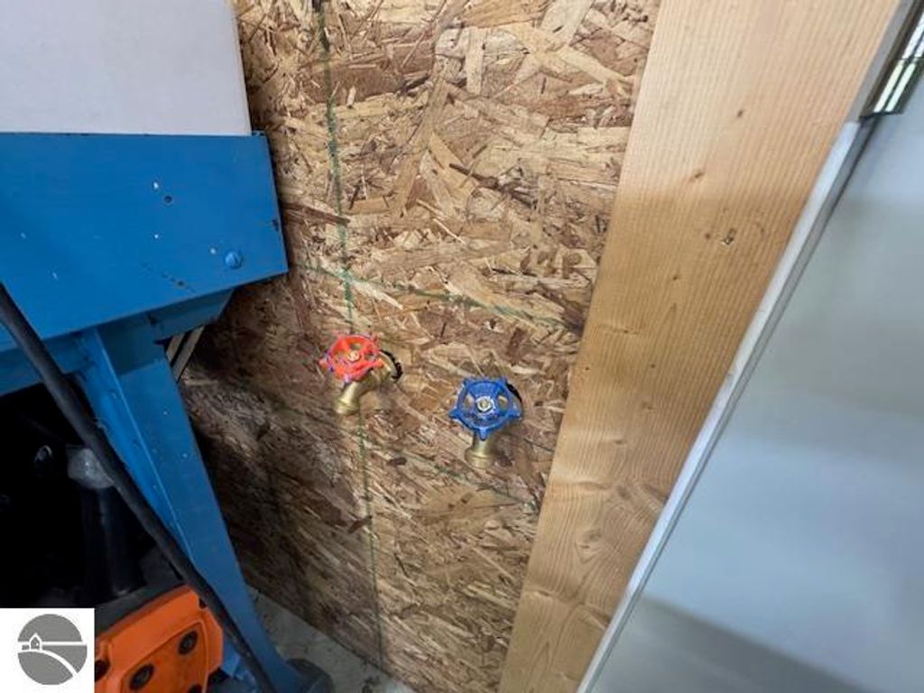 Water access valves on a wooden wall inside a garage, featuring a red valve on the left and a blue valve on the right, with an industrial blue structure partially visible.