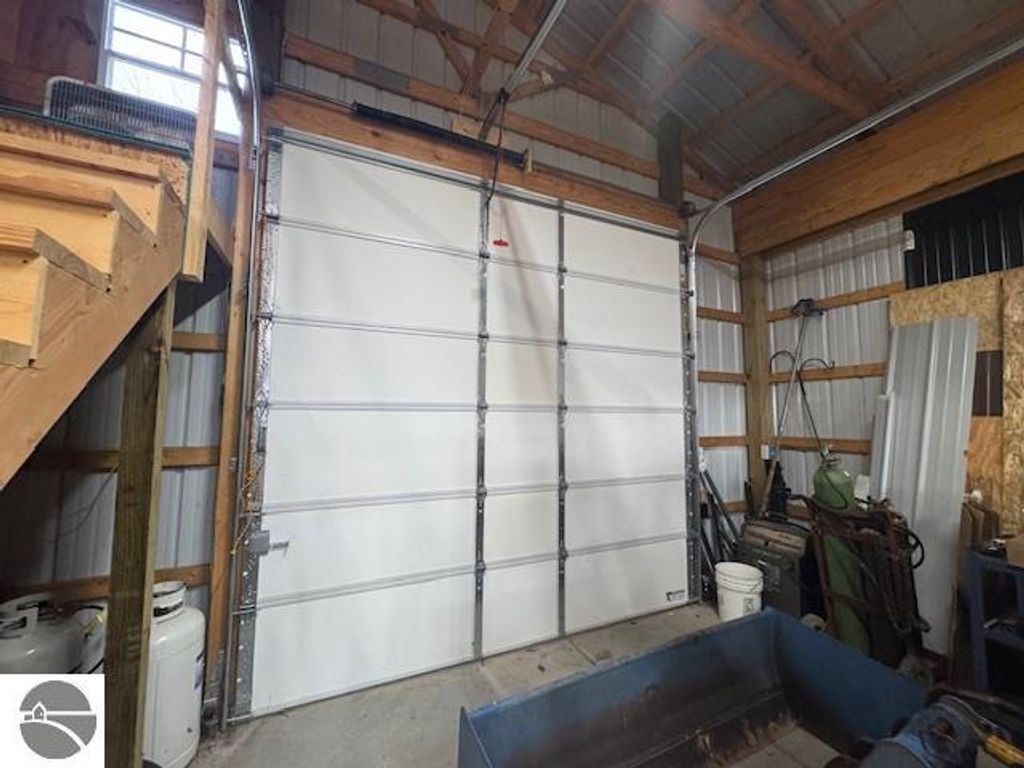 Interior view of a spacious pole barn featuring a large white garage door, wooden beams, and various tools and equipment, highlighting storage potential for vehicles and workspaces on the property at 2520 S Blodgett, Lake City, MI.
