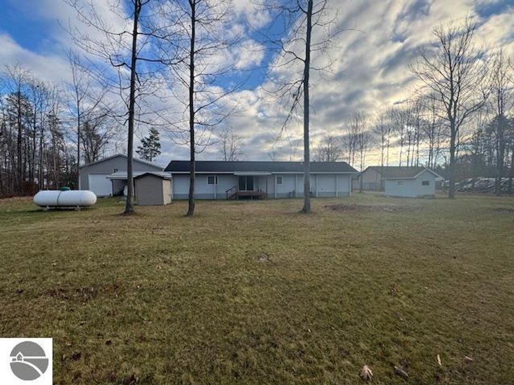 Well-maintained 3-bedroom home with a large yard, surrounded by trees, featuring a propane tank, storage shed, and a clear sky in Lake City, MI.