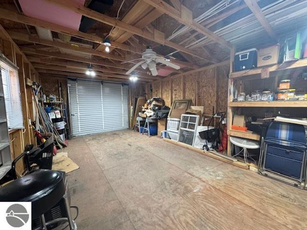 Interior view of a spacious garage with wooden beams, overhead lights, a ceiling fan, and organized storage shelves filled with tools and equipment, showcasing the ample space available for vehicles and storage, relevant to the property listing at 2520 S Blodgett, Lake City, MI.
