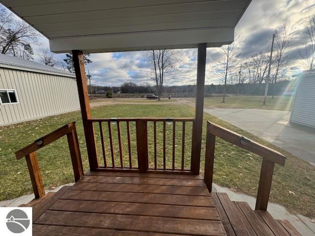 Wooden porch view leading to a spacious yard, showcasing a nearby pole barn and open landscape, emphasizing the property's outdoor space at 2520 S Blodgett, Lake City, MI.