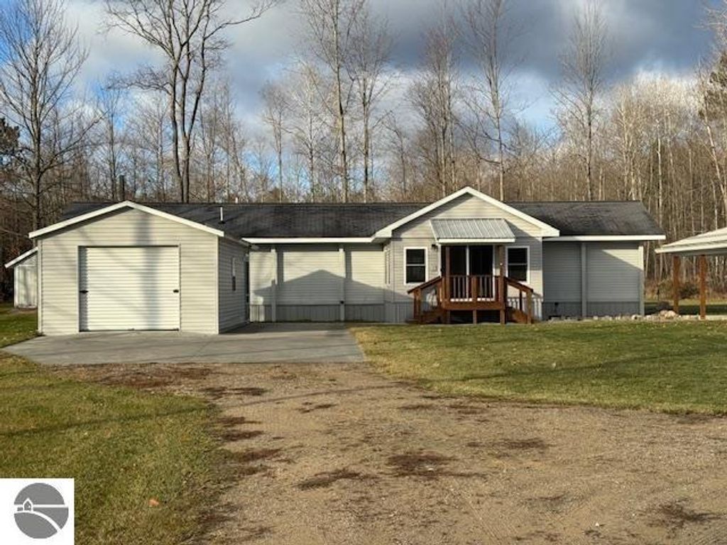 Well-maintained single-story home with a garage, surrounded by trees on 2.5 acres in Lake City, MI, featuring a concrete driveway and welcoming front porch.