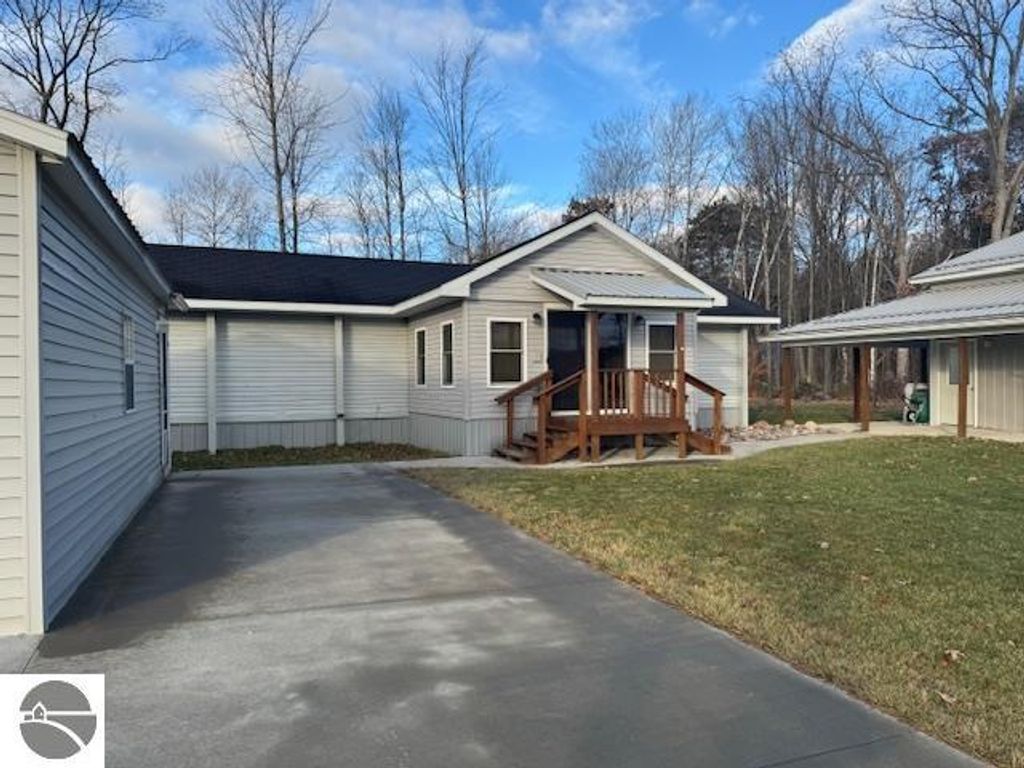 Well-maintained 3-bedroom home with a welcoming porch, surrounded by trees, featuring a concrete driveway and nearby garage, located on 2.5 acres in Lake City, MI.