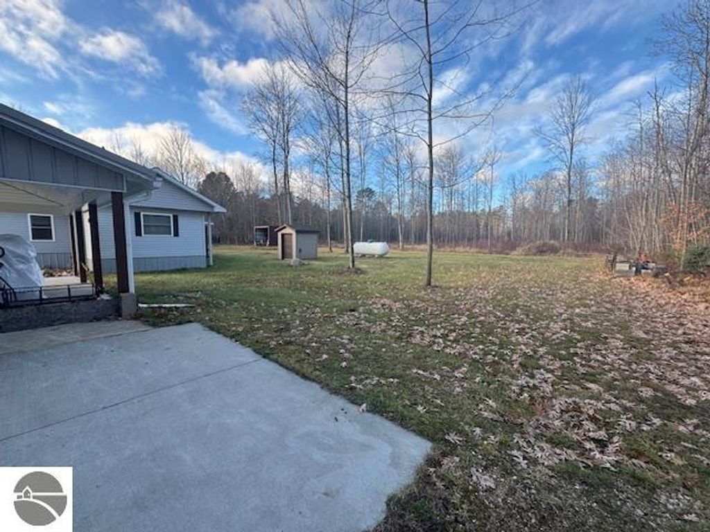 Well-maintained 3-bedroom home exterior on 2.5 acres, featuring a concrete driveway, surrounding trees, and a storage shed in Lake City, MI.