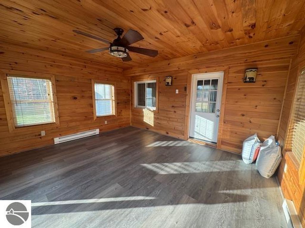 Interior view of a well-lit room with wooden walls and ceiling, featuring a ceiling fan, large windows with blinds, and a door leading outside, showcasing a clean, modern floor suitable for a living space in a Lake City home.