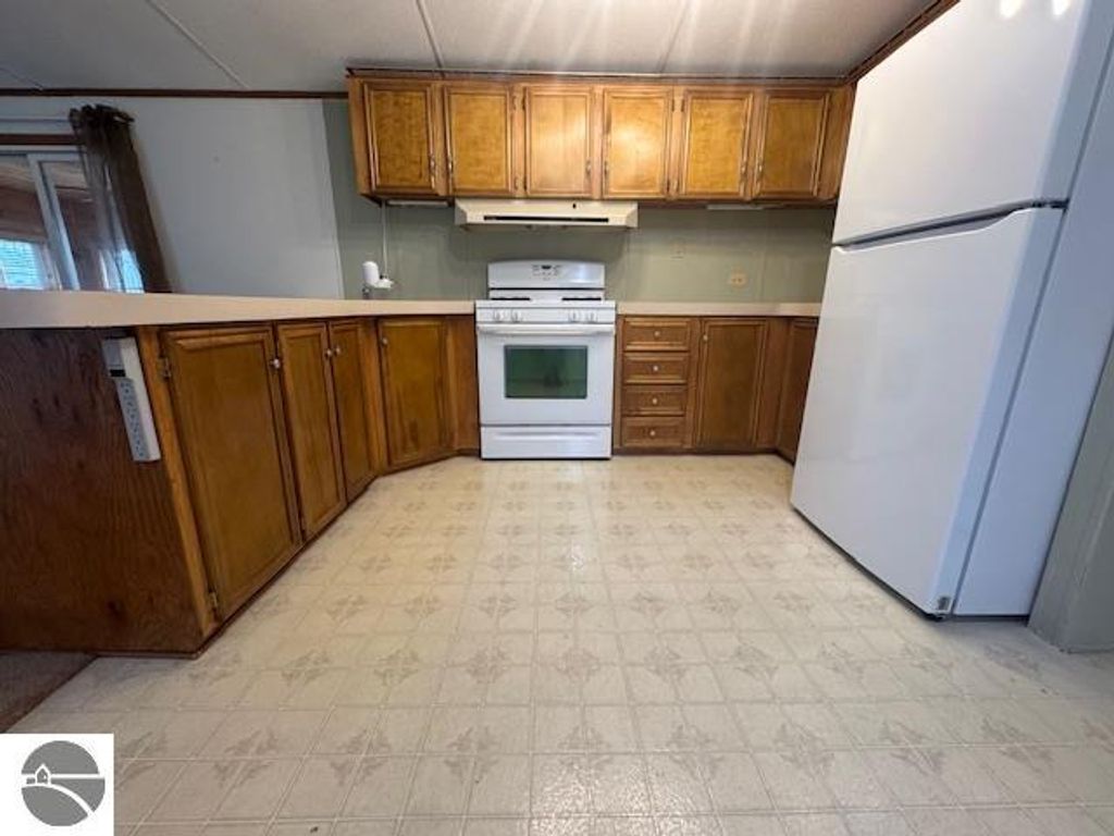 Kitchen interior featuring wooden cabinets, white appliances including a refrigerator and oven, and a tiled floor, showcasing the functional space of the 3-bedroom home for sale at 2520 S Blodgett, Lake City, MI.
