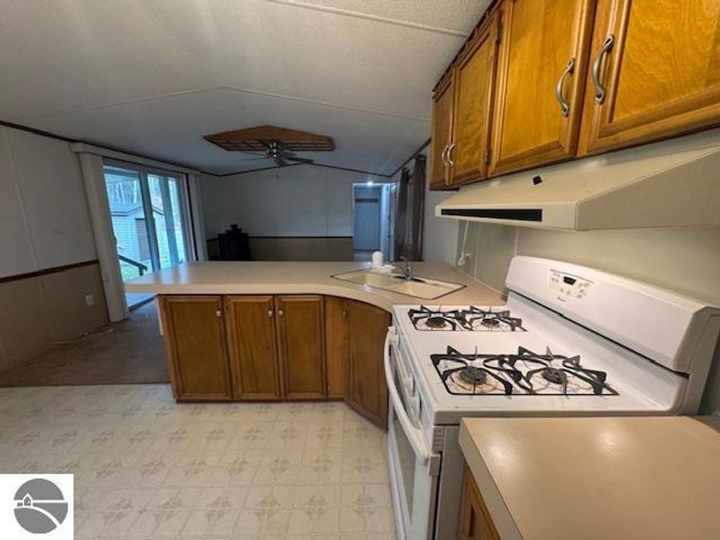 Kitchen interior featuring wooden cabinets, gas stove, and open layout connecting to living area, showcasing the home at 2520 S Blodgett, Lake City, MI, listed for $205,000.
