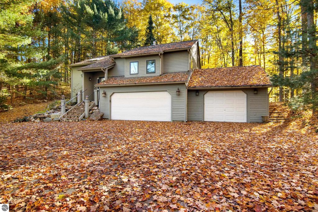 Exterior view of 10371 Deerpath North, Traverse City, MI, showcasing a two-story home surrounded by colorful autumn foliage, featuring a spacious driveway, a three-car garage, and a welcoming entrance with stone steps.