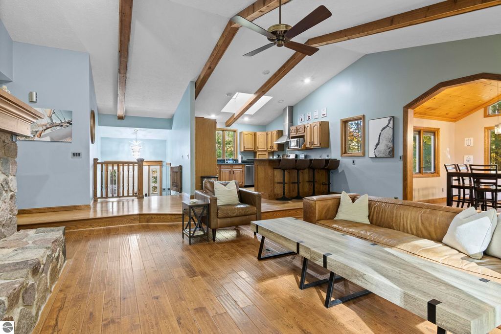 Spacious living area in Traverse City home featuring vaulted ceilings, hardwood floors, modern furnishings, and an open layout connecting to the kitchen and dining spaces.