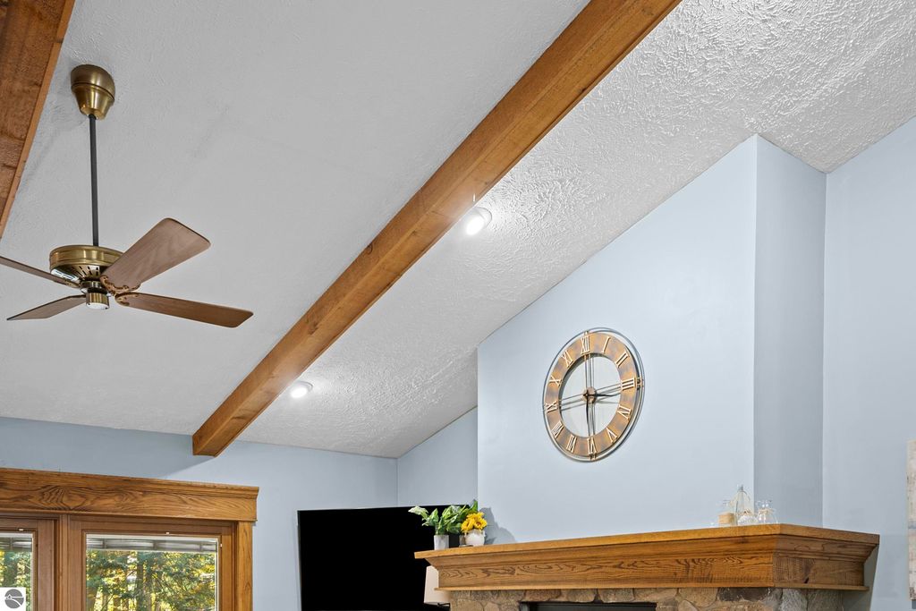 Ceiling featuring a wooden beam, modern ceiling fan, and wall clock in a living space, highlighting the cozy interior of the Traverse City home at 10371 Deerpath North.