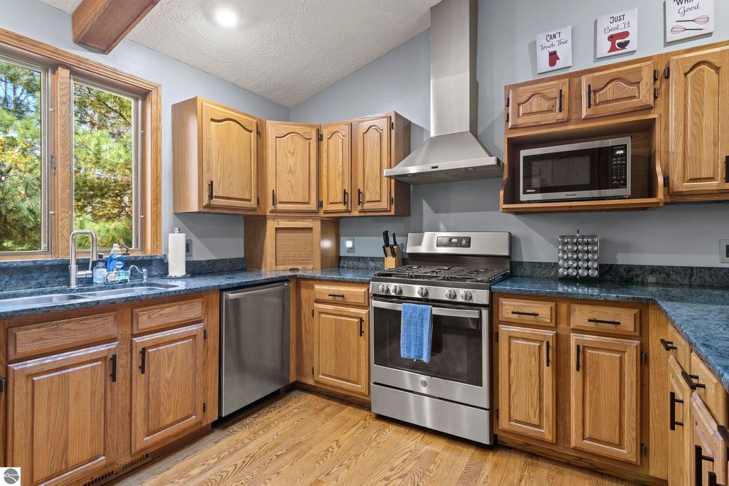 Modern kitchen with wooden cabinets, stainless steel appliances, granite countertops, and large windows showcasing a wooded view, ideal for the luxury home at 10371 Deerpath North, Traverse City, MI.