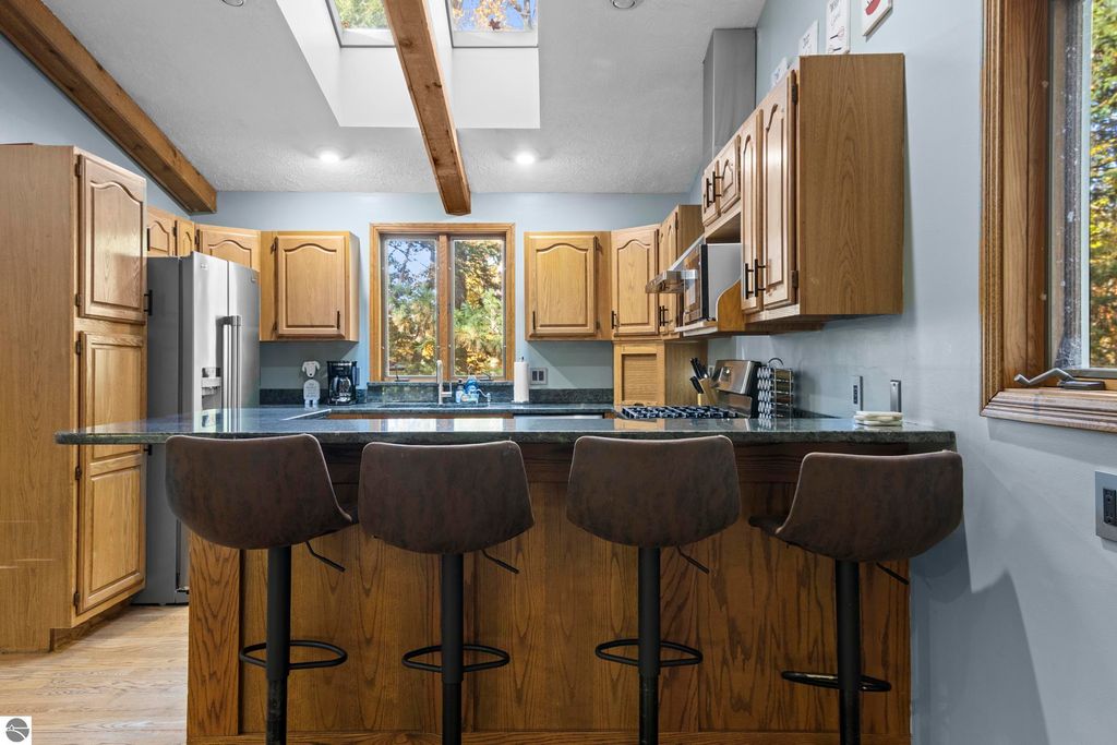 Modern kitchen with wooden cabinetry, granite countertops, and bar seating, showcasing natural light from skylights and windows, highlighting the inviting atmosphere of the home at 10371 Deerpath North, Traverse City, MI.