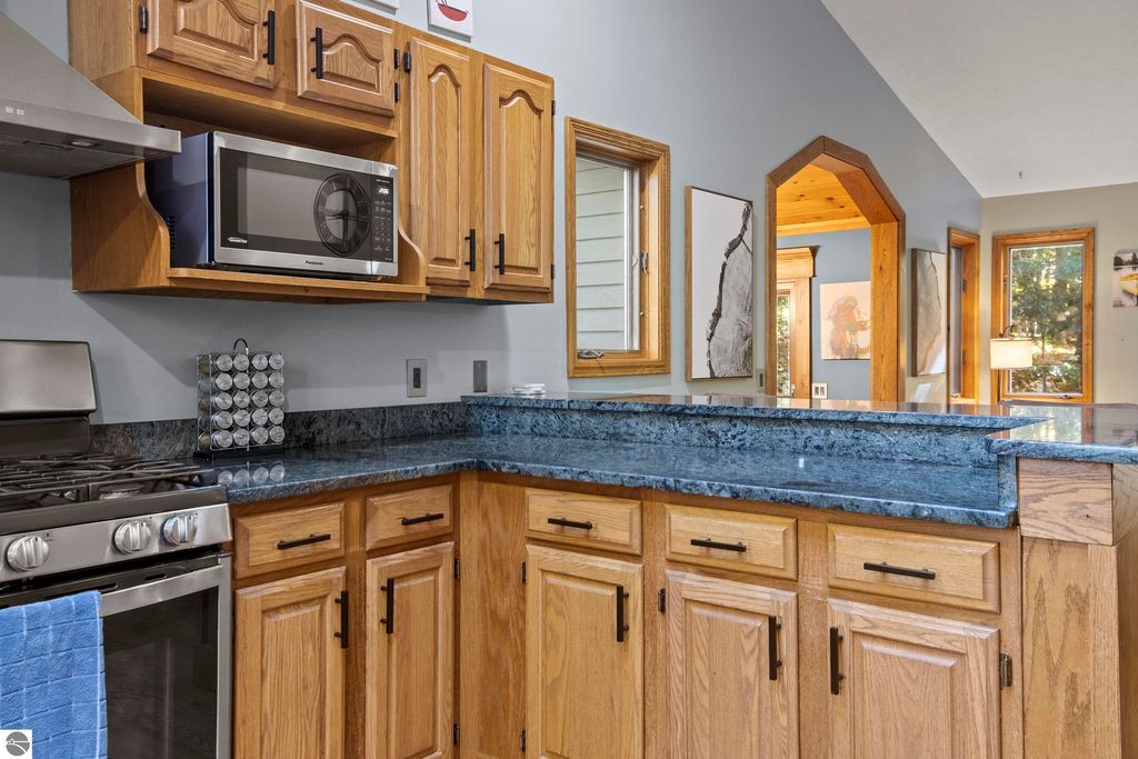 Kitchen interior featuring wooden cabinetry, stainless steel appliances, and granite countertops, showcasing a microwave and a gas stove, with natural light illuminating the space.