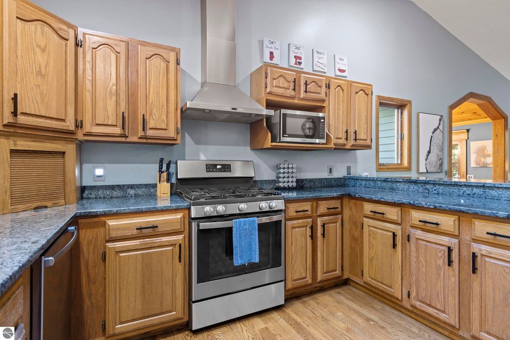 Modern kitchen with oak cabinetry, stainless steel appliances, granite countertops, and a view into the adjoining living space at 10371 Deerpath North, Traverse City, MI.
