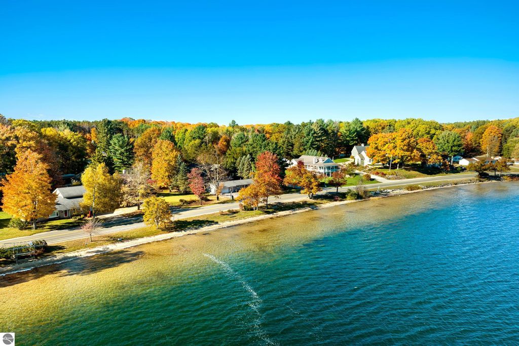 Aerial view of waterfront property at 10371 Deerpath North, Traverse City, showcasing autumn foliage, sandy beach, and homes along Long Lake.