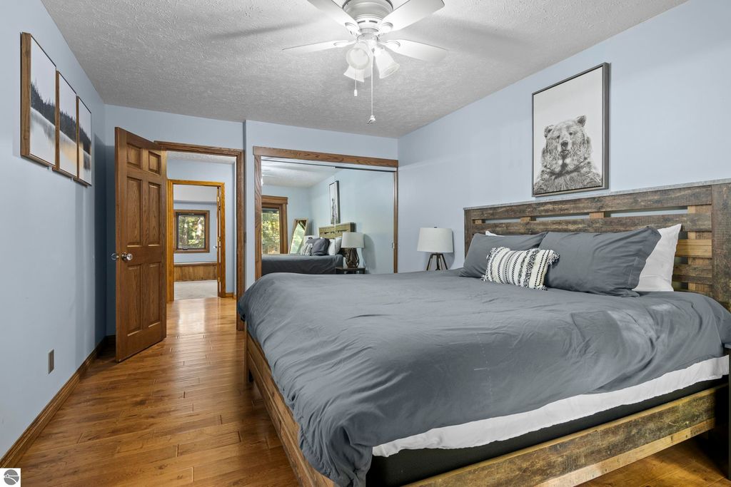 Cozy bedroom featuring a wooden bed frame with gray bedding, a bear portrait on the wall, and natural light from windows, showcasing a serene and inviting atmosphere in the Traverse City home at 10371 Deerpath North.