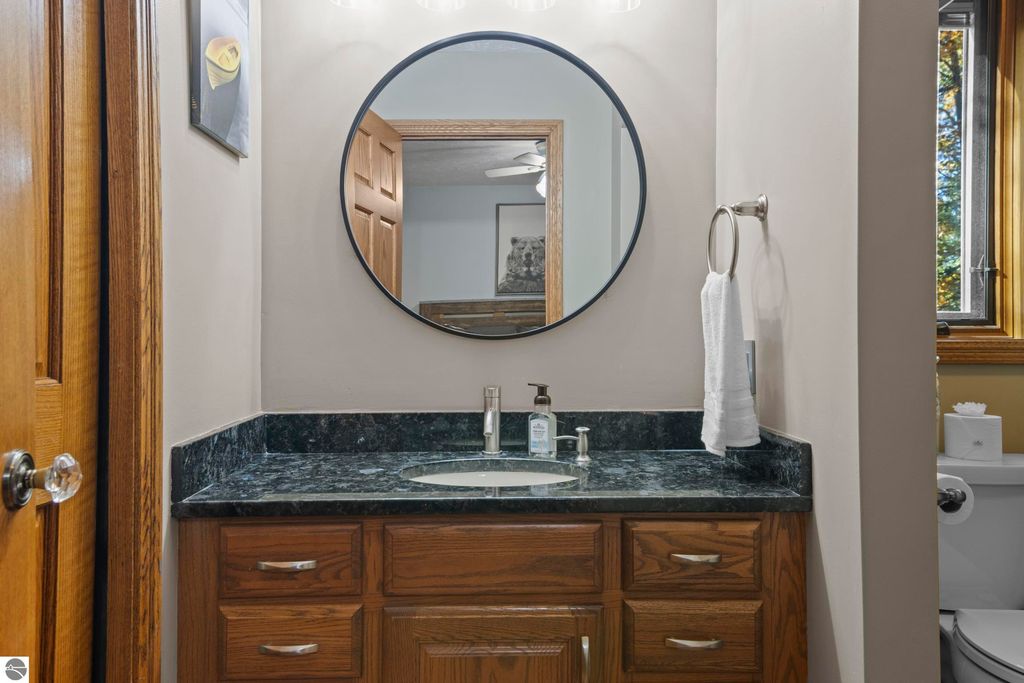 Modern bathroom vanity with dark granite countertop, round mirror, wooden cabinetry, and natural light from window.