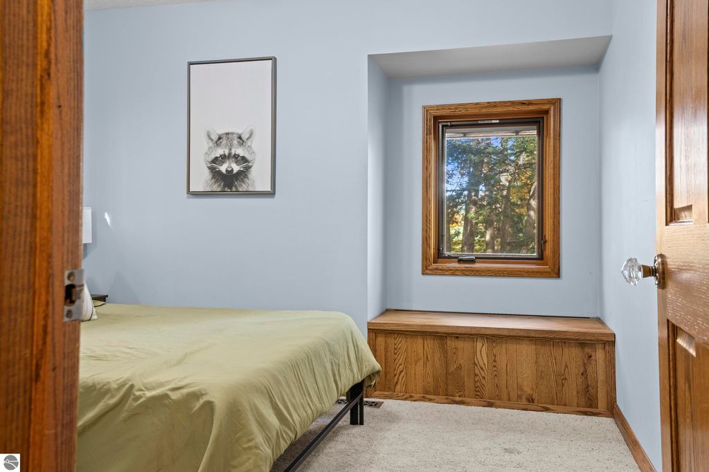 Cozy bedroom featuring a green bedspread, raccoon artwork on the wall, and a window with wooded views, showcasing a serene atmosphere in a Traverse City home.
