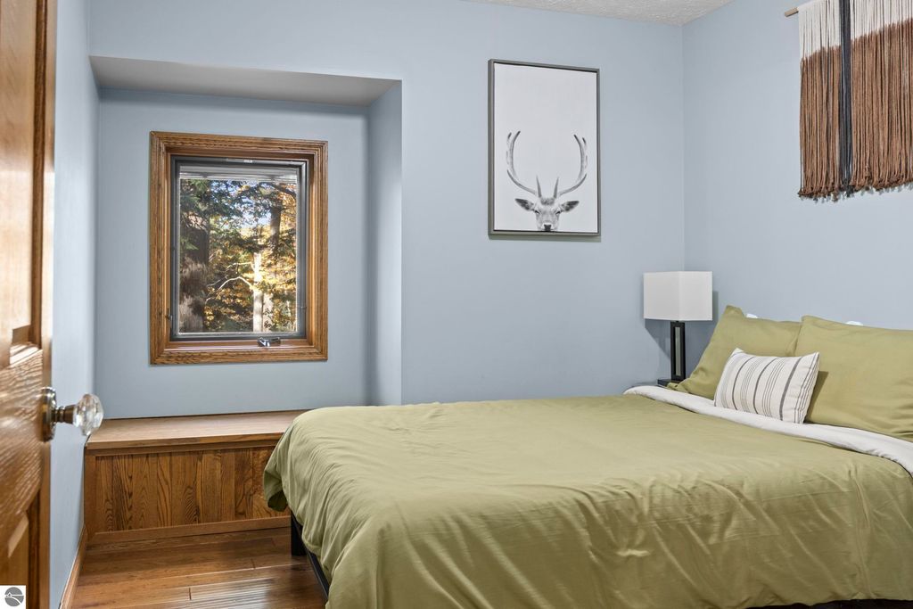 Cozy bedroom with green bedding, wooden window seat, and nature-themed wall art, showcasing serene views of the surrounding forest.