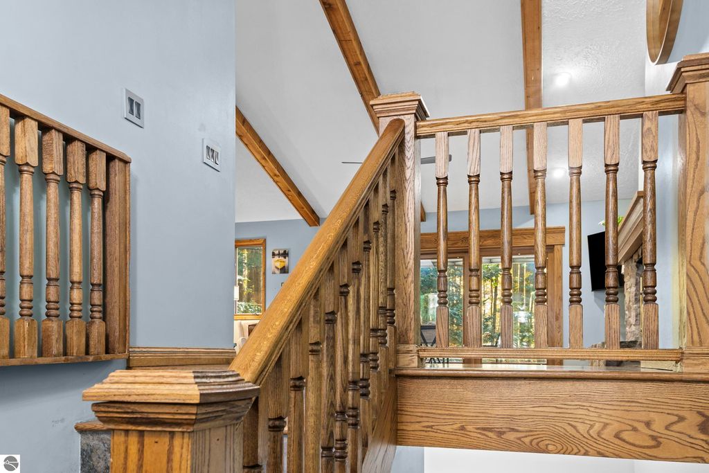 Wooden staircase with decorative railings leading to a light-filled upper level, featuring natural wood elements and a view of the living area, showcasing the spacious and inviting interior of the home at 10371 Deerpath North, Traverse City, MI.