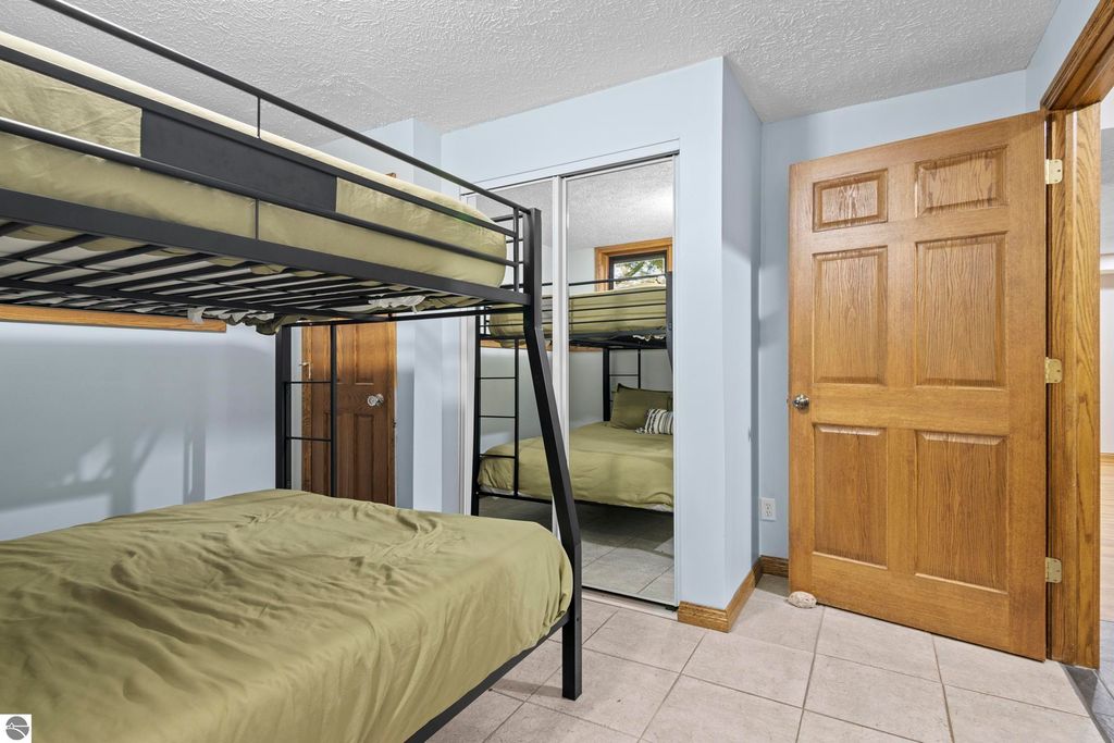Bunk beds with green bedding in a cozy bedroom featuring a mirror, wooden door, and light blue walls, showcasing space for guests in a Traverse City home listing.